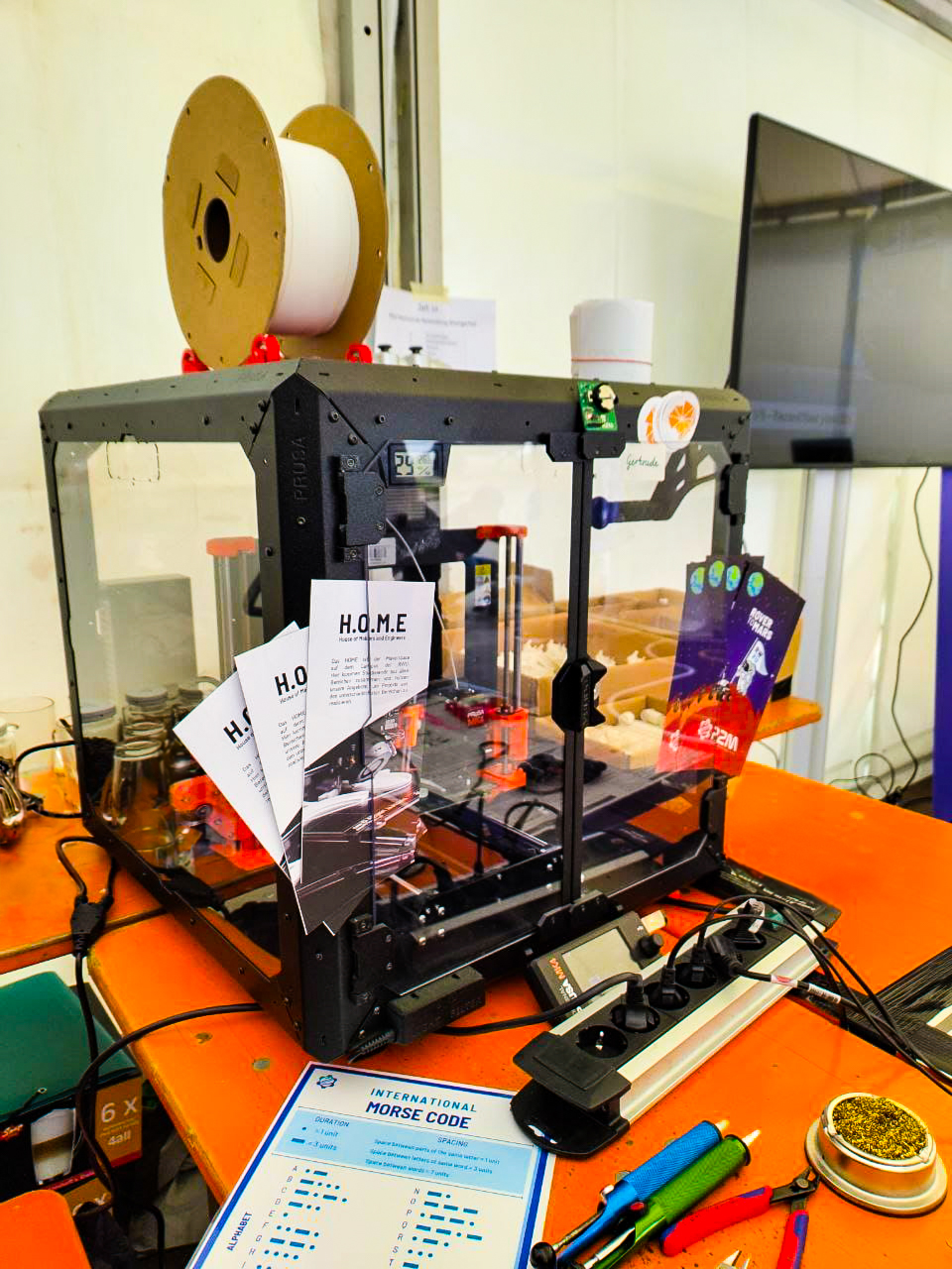 Der MK4 Drucker, gefüllt mit HOME Flyern, steht auf seinem Messe Tisch mit dem Morse-Code Zettel der Rover to Mars