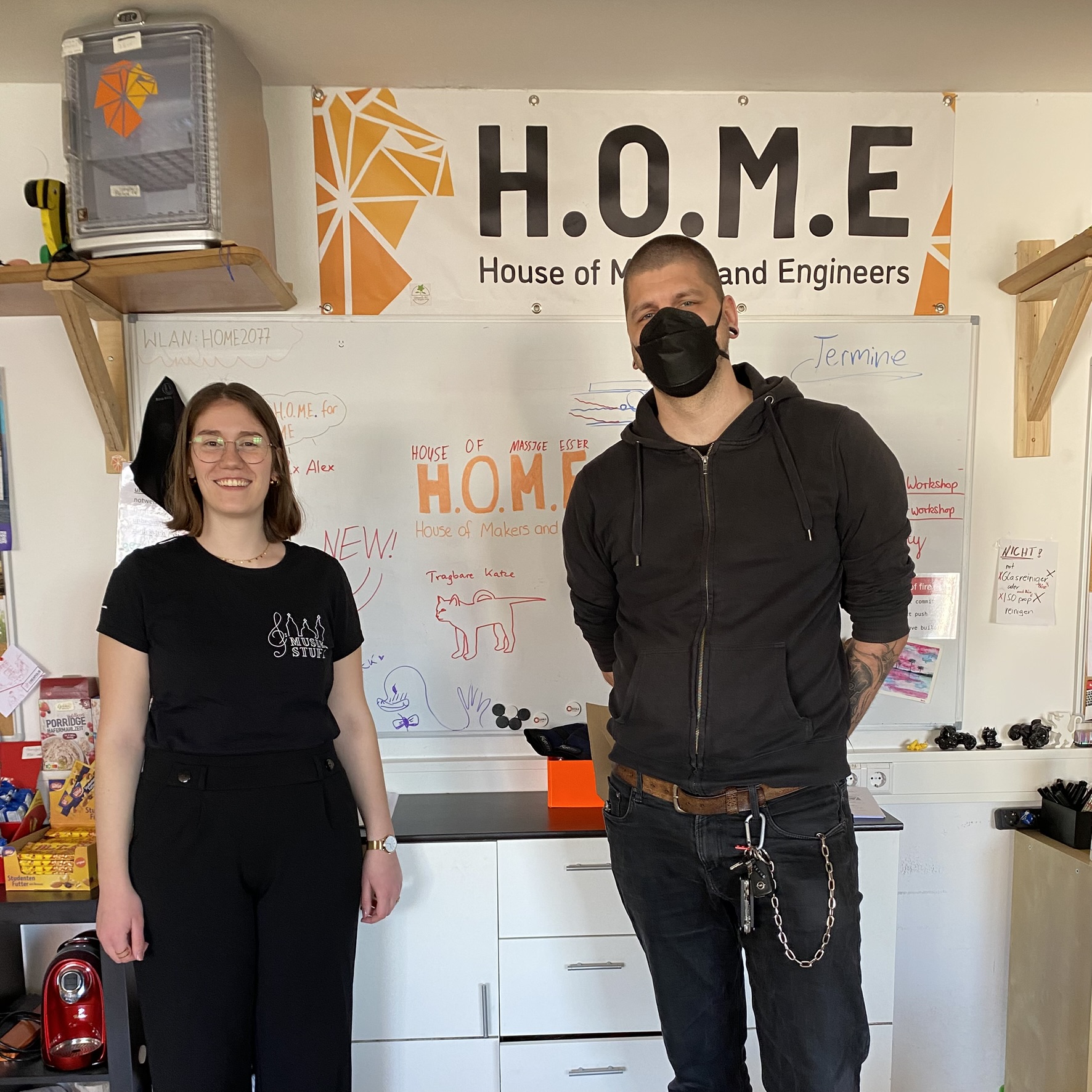 Das Bild zeigt zwei Personen vor dem Banner des H.O.M.E.
