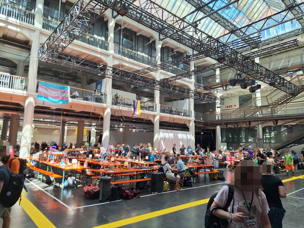 Die GPN-Halle morgens, relativ menschenleer. Es stehen viele Zeltgarnituren mit aufgebauten Rehnern, Servern und Menschen, die daran arbeiten oder frühstücken