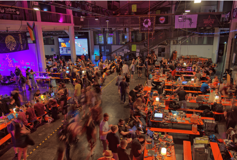Ein Bild der GPN21, es zeigt das Hackcenter, an welchem Menschen an Zeltgarnituren sitzen und an ihren Projekten arbeiten.